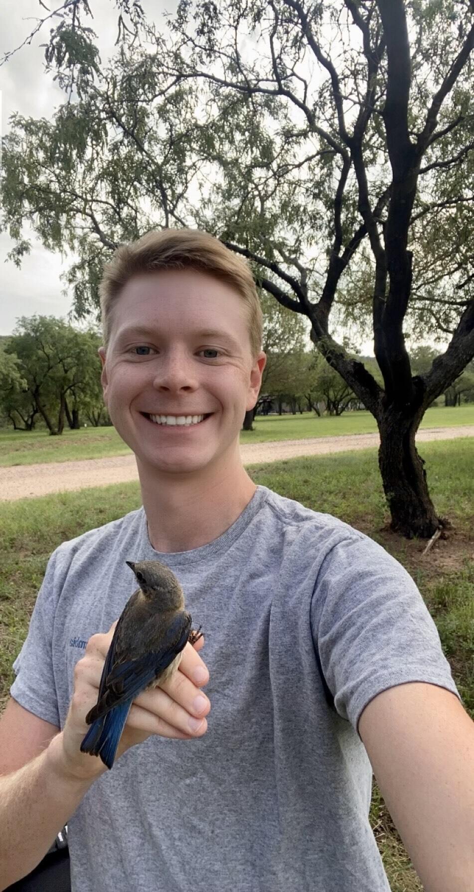 Smiling under the canopy of a large mesquite tree, Matt Jenkins holds an Eastern (Azure) Bluebird.