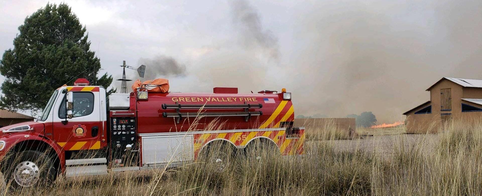 A wildland firefighting truck sits in front of AWRR's headquarters buildings as smoke billows into the sky from the surrounding grasslands.